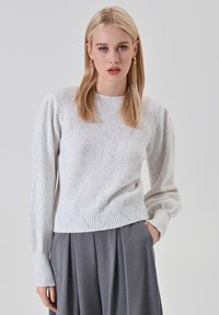 Maglione lavorato a maglia grigio chiaro con vita a coste, maniche lunghe a sbuffo e dettagli a pois. Abbinato a pantaloni grigi a pieghe.