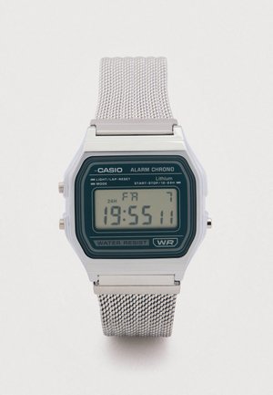 Digitalna ura Casio z zelenim številčnico, srebrnim mrežnim paščkom, kvadratno ohišje, odporna na vodo, ima funkciji alarma in kronografa.