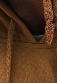 Brauner Hoodie aus strukturiertem, gestricktem Stoff. Verfügt über eine Kordel am Kragen und eine sichtbare innere Schicht, die heller gefärbt ist.