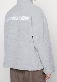 Grau gefütterte Jacke mit hohem Kragen, mit einer weichen, strukturierten Oberfläche und dem Wort "PEGADOR" in Weiß auf dem Rücken.