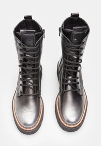 Bottes en cuir noir à lacets avec une finition brillante, présentant une semelle de couleur brun clair contrastante et des coutures détaillées le long du bord.