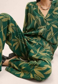 Green fabric outfit with a leaf pattern in gold, featuring a collared top and wide-leg pants. Textured, lightweight material.