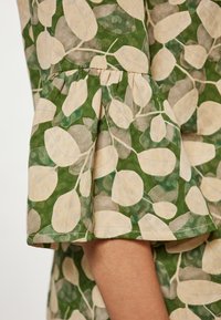 Blusa verde con stampa a motivo foglia in beige e verde chiaro, con maniche arricciate e una texture morbida.