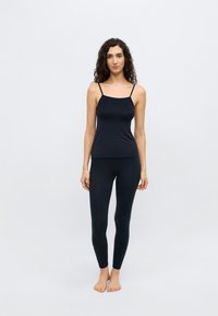 Zwarte naadloze tanktop met dunne bandjes, gecombineerd met hoog getailleerde zwarte legging. Gladde textuur, aansluitend ontwerp, minimalistische stijl.