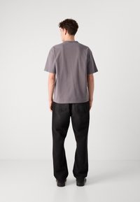 Chemise grise à manches courtes avec une coupe décontractée, associée à un jean noir ample, présentée de dos sur un fond clair.