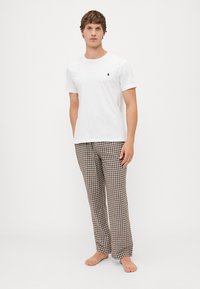 Witte korte mouwen t-shirt met een klein logo, gecombineerd met bruin en beigeruitjes pyjamabroek, beide in een relaxte fit.