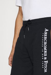 Shorts neri in cotone con vita regolabile tramite cordino, con testo bianco "Abercrombie & Fitch" e "Fondato a New York" sul lato.