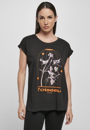 Black cotton T-shirt with rolled sleeves, featuring a colorful bird and plant design in pink and orange, text reads "l'oiseau de paradis."