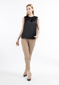 Sort satin sld blouse med rund halsudskæring, parret med beige slim-fit bukser og sorte hæle med guldaccent.