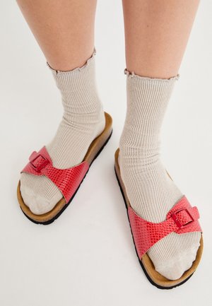Røde sandaler med slangeskindsmønster, brede remme og spænde, kombineret med lysebeige ribstrikkede sokker. Flad sål med brun bund.
