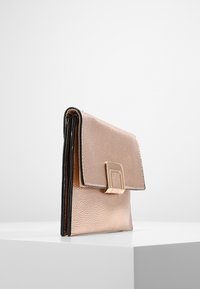 Plånbok i roséguld med textur av läder och rektangulär lås, som har en elegant design och kontrasterande svart trim längs kanterna.