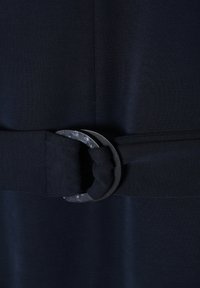 Ciemnoniebieska tkanina o teksturowym wykończeniu, z paskiem ze węzłem, zabezpieczonym okrągłą metalową klamrą w wzór w kropki.