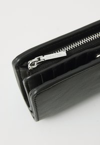 Black leather wallet with silver zip, multiple card slots, and Calvin Klein branding on the zipper pull. Textured finish, rectangular shape.