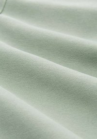 Helles, grünes, weiches Material mit feiner Strickstruktur und sanften Falten, die eine glatte, fließende Oberfläche erzeugen.