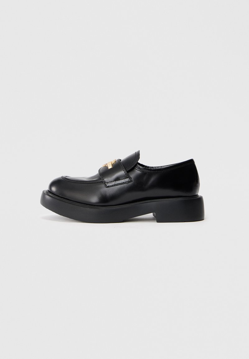 Shoe de couro preto com bico arredondado, sola de plataforma baixa e acessórios dourados decorativos na aba. Textura suave com design minimalista.