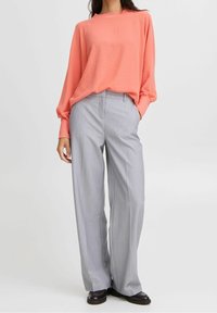 Maglietta a maniche lunghe color corallo con una vestibilità morbida, abbinata a pantaloni larghi a vita alta grigio chiaro con sottili righe verticali.