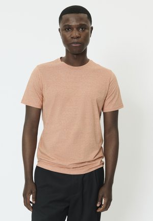 Kortærmet, rundhalset t-shirt i lyse koralfarvet stof med en meleret tekstur. Kombineret med sorte bukser, vist mod en hvid baggrund.