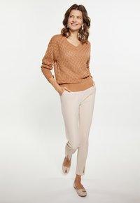 Jasnobrązowy sweter dzianinowy z dekoltem w kształcie litery V i wzorem w romby, zestawiony z beżowymi spodniami slim-fit. W zestawie płaskie, cieliste baleriny.