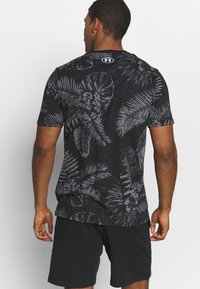 Černé triko s krátkým rukávem s šedým vzorem tropického listí, vyrobené z měkkého materiálu. Má kulatý výstřih a logo Under Armour na zadní straně.
