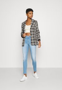 Blazer a cuadros en blanco y negro sobre un top corto claro, combinado con jeans ajustados de color azul claro y zapatillas blancas. Tejido suave, ajuste entallado.