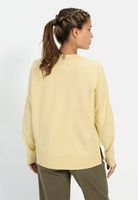 Lichtgele sweatshirt met lange mouwen, geribbelde manchetten en een hoge halslijn. Beschikt over een contrasterend zilveren ritsdetail aan de achterkant.