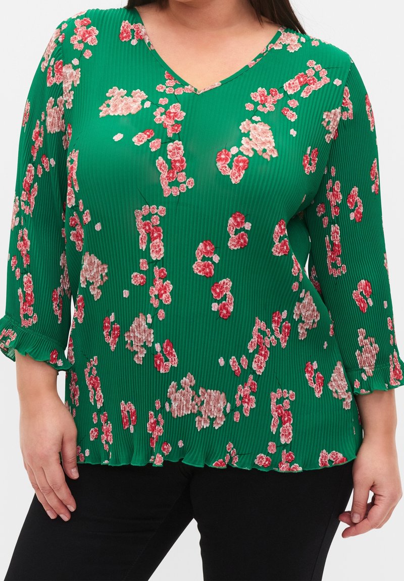 Top plissettato verde con scollatura a V, caratterizzato da motivi floreali rosa e bianchi, maniche a tre quarti e vestibilità ampia.