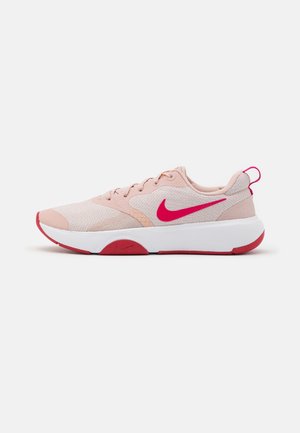Sneakers basses Nike rose et beige avec logo Swoosh rouge, semelle blanche épaisse et accents rouges sur la semelle extérieure et l'onglet du talon.