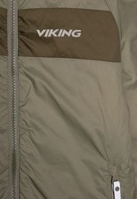 Veste matelassée verte Viking avec une bande horizontale marron, un logo argenté, une fermeture éclair et des accents élastiques aux poignets et à l'ourlet.