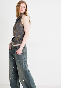 Top cinza camuflado sem mangas com um decote alto e a parte inferior franzida, combinado com jeans de denim leve e solto em azul claro com tachas metálicas e buracos.