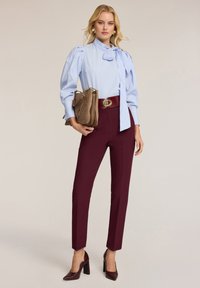 Blauw en wit gestreepte blouse met strikdetail, gecombineerd met slim-fit burgundy broek en een bruine handtas. Bruine hakken maken de look af.