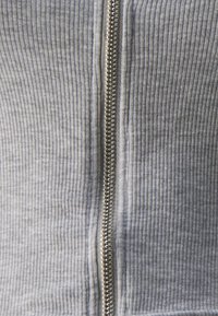 Tessuto grigio a coste con chiusura a zip. Presenta una superficie texture e sottili linee verticali. La zip è metallica e si trova al centro.