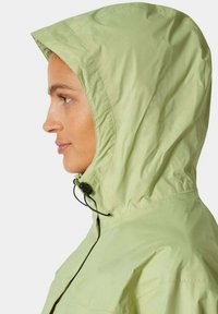 Jasnozielona kurtka przeciwdeszczowa z kapturem, z możliwością regulacji za pomocą sznurka, gładka w dotyku, z widocznymi detalami przeszycia.