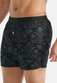 Černé plavecké šortky s květinovým vzorem v tmavě šedé barvě, vybavené elastickým pasem a malým kovovým knoflíkem.