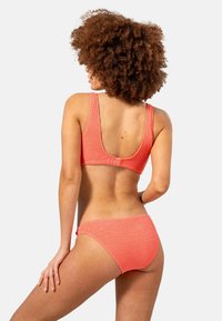 Korallfärgad bikini set som har en texturerad, rygglös bh med breda axelremmar och matchande trosor, som visar en slät yta och en åtsittande design.