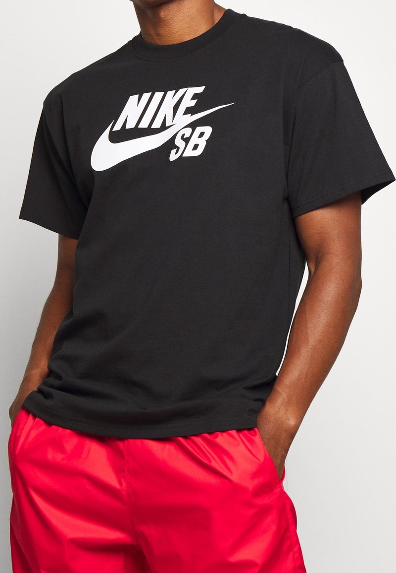 Černé bavlněné tričko s velkým bílým logem "NIKE SB" na přední straně. Krátké rukávy a kulatý výstřih. Hladká textura, volný střih.