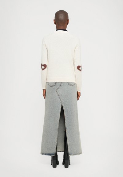 Cream knitted cardigan with heart patches on elbows, paired with a long gray denim skirt featuring a back slit and black heeled boots.