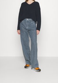 Navy ribbad tröja med V-hals, kombinerad med ljusblå vida jeans. Svarta och orange sneakers fulländar outfiten. Enkel, avslappnad stil.