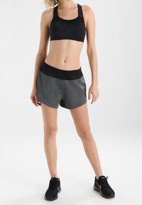 Zwarte sport-beha en grijze sportshorts met een brede zwarte tailleband, met een gladde textuur en gebogen zoom. Zwarte sneakers maken de outfit compleet.