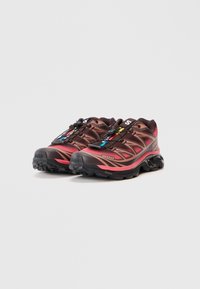 Παπούτσια trail running σε καφέ και ροζ, με υφή στην επιφάνεια, ενισχυμένο δάκτυλο και σύστημα γρήγορης κορδόνωσης με πολύχρωμες λεπτομέρειες.