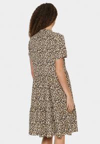 Kurzärmeliges, knielanges Kleid in Beige mit schwarzem Leopardenmuster. Verfügt über einen gestuften Rock und einen runden Ausschnitt. Weicher Stoff.
