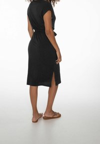 Robe midi noire côtelée avec manches courtes et fente latérale. Texture douce, taille ceinturée et ourlet à hauteur du genou. Portée avec des sandales plates.