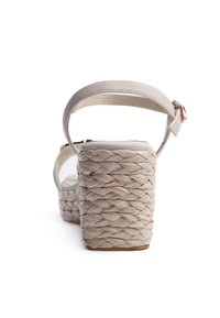 Sandalia de cuña beige con plataforma de paja trenzada, correa ajustable en el tobillo y parte superior de cuero suave. Plantilla ligeramente acolchada.