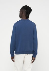 Φούτερ ναυτικ ού μπλε με στρογγυλή λαιμόκοψη, μακριά μανίκια, ριμπ μανσέτες και τελείωμα. Λείος υφής, χωρίς ορατά σχέδια ή μεταλλικά στοιχεία.