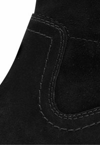 Botín negro de ante hasta el tobillo con una textura suave, que presenta costuras en contraste y un diseño curvado delineado en el lateral.