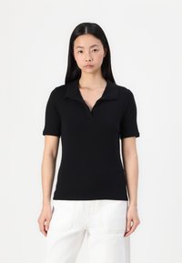 Polo noir à manches courtes avec un col et une silhouette ajustée, fabriqué en tissu à texture lisse. Associé à un pantalon blanc.