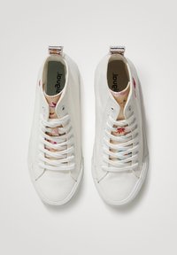 White canvas sneakers with round toes, flat laces, and floral-patterned inner lining. Features a striped pull tab at the heel.