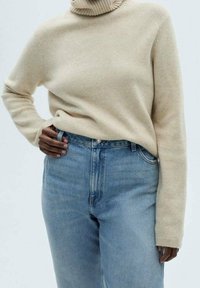 Pull à col roulé beige en tissu doux associé à un jean taille haute bleu clair. Comprend un col côtelé et une finition texturée.