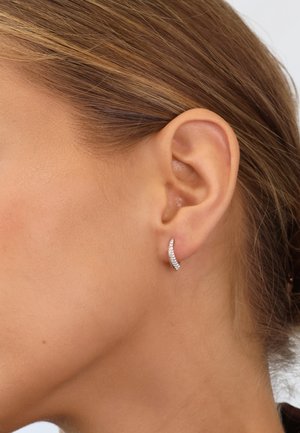 Silberne, geschwungene Ohrringe mit einer Reihe kleiner, klarer Kristalle, die eine polierte Textur und ein minimalistisches Design aufweisen. Geeignet für verschiedene Anlässe.