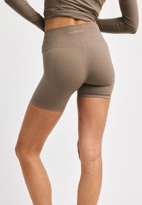 Brune idrettsshorts med høy midje. Laget av glatt stoff, med en logo på baksen og en tettsittende design.