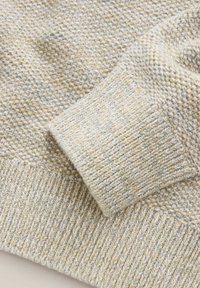 Tessuto lavorato a maglia di colore chiaro con un motivo testurizzato, con un polsino a coste in tonalità contrastanti di crema, beige e sottili screziature blu.